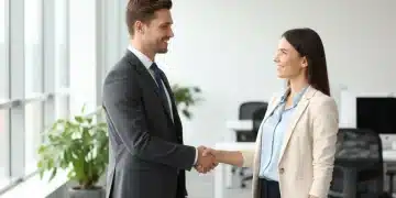 Homem e mulher em entrevista de emprego em 2026, apertando as mãos com confiança.